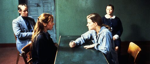Zwei Frauen sitzen sich im Gefängnis an einem Tisch gegenüber. Im Hintergrund sitzt ein Anwalt und eine Wärterin. 