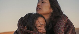 Zwei junge Frauen in der Steppe umarmen sich eingehüllt in eine Decke.