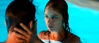 Eine junge Frau und einer junger Mann im Pool. Die Frau hält mit beiden Händen das Gesicht des Mannes.