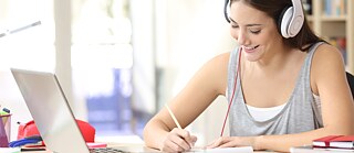 Young woman at desk with headphones and laptop