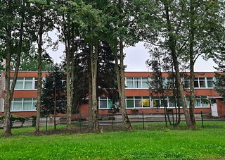 Dviaukštis pastatas, kuriame įsikūręs vaikų darželis, priekyje pieva ir medžiai