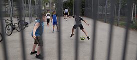 Auf einem umzäunten Platz spielen einige Kinder Fußball.