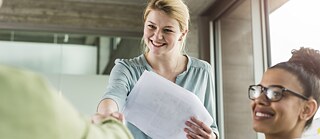 Eine junge Frau schüttelt jemand im Büro die Hand