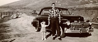 1950s photo showing a father posing with his young daughter in front of a vintage car