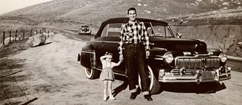 Aufnahme aus den 1950er Jahren, in der ein Vater mit seiner kleinen Tochter vor einem Oldtimer posiert