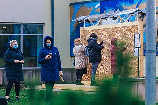 Im Innenhof steht eine Wandinstallation aus Plexiglasgerüst, in das Holzklötze mit eingravierten Zitaten eingesetzt sind. Leute wähle die Holzklötze aus.