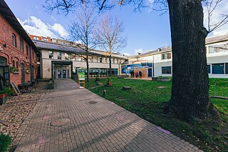 Im Innenhof steht eine Wandinstallation aus Plexiglasgerüst, in das Holzklötze mit eingravierten Zitaten eingesetzt sind. Leute wähle die Holzklötze aus.