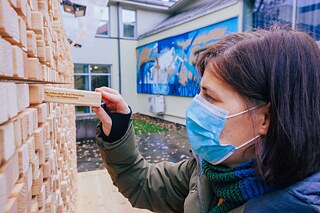 Eine Wandinstallation aus Plexiglasgerüst, in das Holzklötze mit eingravierten Zitaten eingesetzt sind. Eine Frau zieht einen Holzklotz aus.