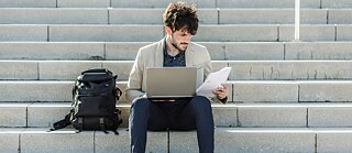 Person sitzt auf einer Treppe und sieht sich Angebote an auf Laptop an