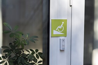 Eingang mit Türklingel und Hinweisschild für Rollstuhlrampe