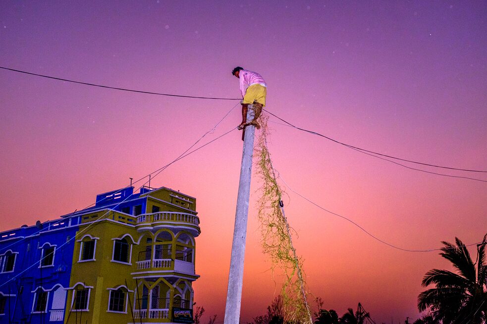 Nachdem der Wirbelsturm Bulbul in der Region Südbengalen eine Spur der Zerstörung hinterlassen hat, repariert ein Bewohner eine elektrische Leitung. Bakkhali, Indien. 2019.