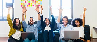 Lerner-Gruppe mit Laptop vor dem Sofa freut sich