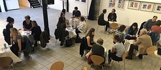 Menschen reden miteinander, an kleinen Tischen sitzend