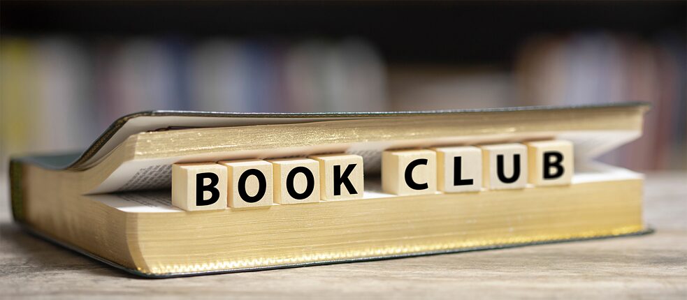 Zwischen die Seiten eines Buches sind kleine Buchstabenklötze mit der Aufschrift Book Club eingeklemmt. 