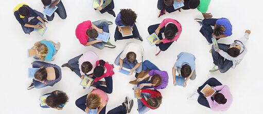 Eine Gruppe Schüler und Schülerinnen sitzen am Boden und lernen mit Tablets und iPads.
