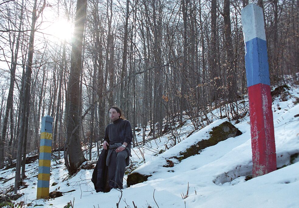Arpád Soltész medzi hraničnými kameňmi na zelenej ukrajinsko-slovenskej hranici, presne v okamihu, keď minister vnútra Vladimír Palko kontroluje jej „hermetickú nepriepustnosť". Asi 2005.
