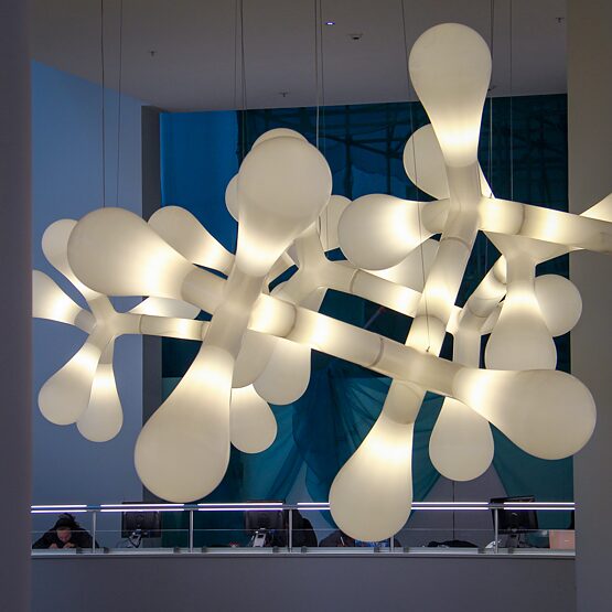 Ein Kunstwerk aus mehreren großen Lampen hängt von einer Decke in einem Ausstellungsraum. 