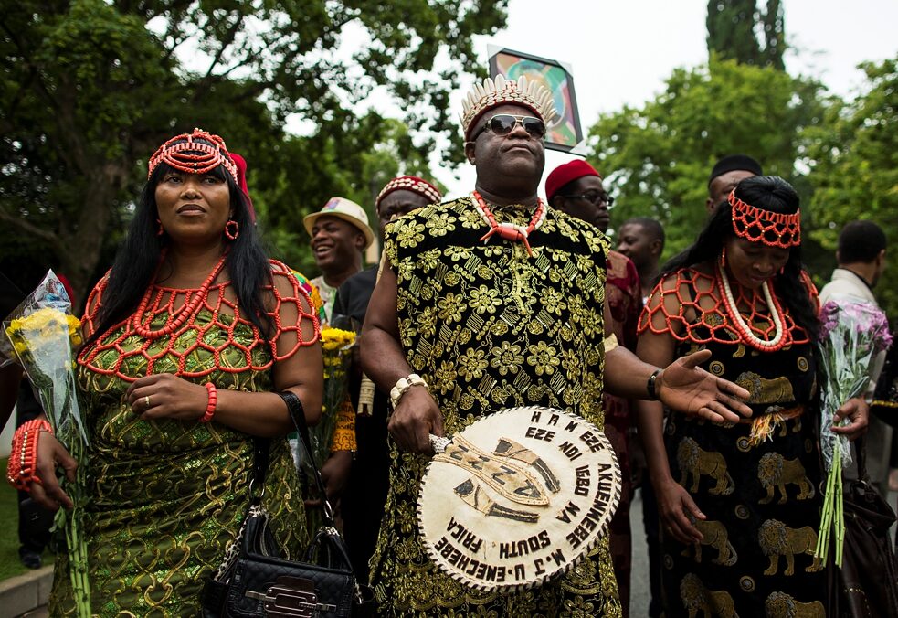Dekolonisation – Nigerianer*innen vom Stamm der Igbo in traditioneller Kleidung versammeln sich am 9. Dezember 2013 vor dem Haus des damals gerade verstorbenen südafrikanischen Präsidenten Nelson Mandela in Johannesburg, Südafrika, um der Anti-Apartheid-Ikone Respekt zu zollen.
