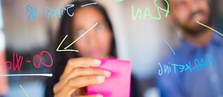 Businesswoman working behind a transparent screen with a sticky note and a hand-painted coloured chart