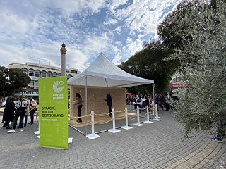 The installation at Sarayönü Square, in front of the Dikilitas column, under an awning. In front of it is the banner of the Goethe-Institut and next to it are groups of people.