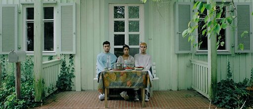 three young people sit on a bench in front of a house