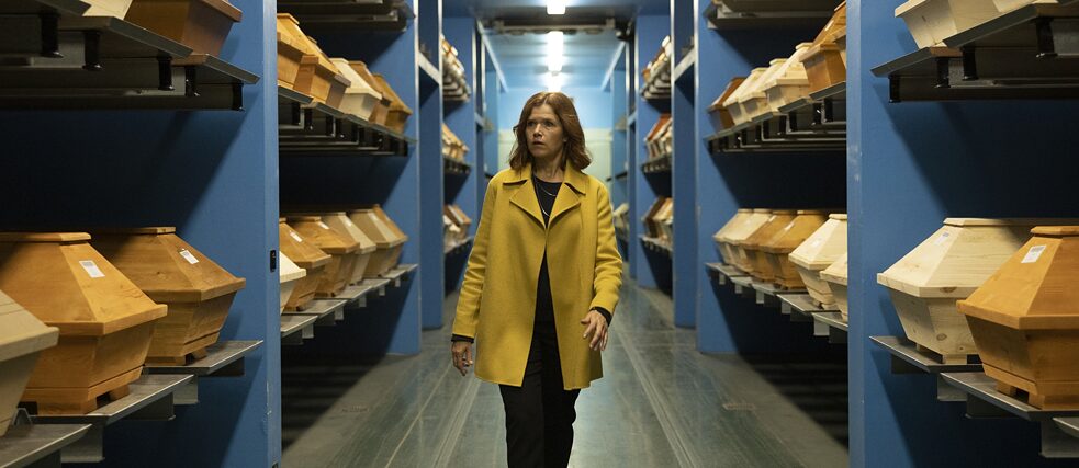 Standbild aus der Netflix Serie Standbild aus der Netflix Serie "Das letzte Wort": Karla Fazius (Anke Engelke) spaziert in einem Krematorium durch einen Flur gefüllt mit Regalen voller neuer Särge.