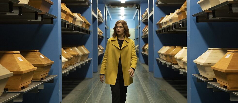 Still frame from the Netflix Serie "The last word": Karla Fazius (Anke Engelke) in the cremtory, walking through a hallway which is filled with shelves full of new coffins.