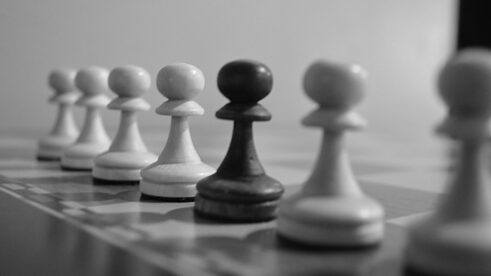 In der Mitte einer Reihe weißer Schachfiguren steht eine schwarze Figur.
