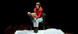 Deborah Weber liest ein Buch, während sie auf einem Stuhl sitzt. Vor ihr werden Kissen auf den Boden gelegt.