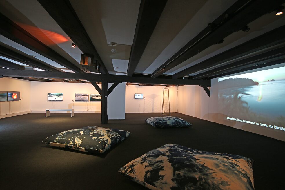 Eine audiovisuelle Installation mit großen Sitzkissen am Boden in einer Galerie