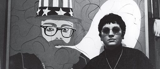 Bild aus dem Film PARIS CALLIGRAMMES von Ulrike Ottinger: eine kurzhaarige Frau mit einer runden Sonnenbrille steht vor einem Wandbild