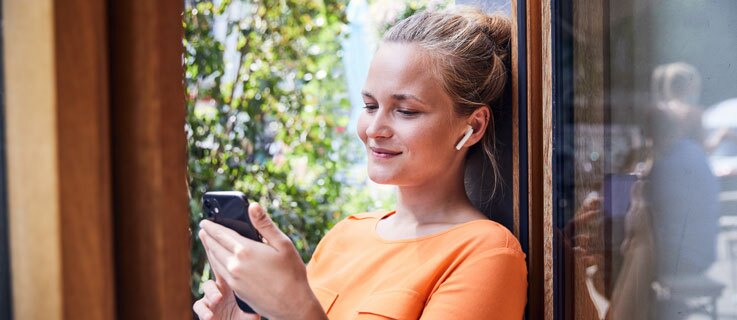 Junge Frau tippt mit dem Finger auf den Screen ihres Smartphones und lächelt.