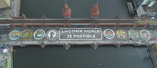 Hoopvol: “Eine andere Welt ist möglich” (“Een andere wereld, het kan”), zo luidt de oproep die activisten in reuzegrote letters op de Oberbaumbrücke in Berlijn hebben geschilderd. 
