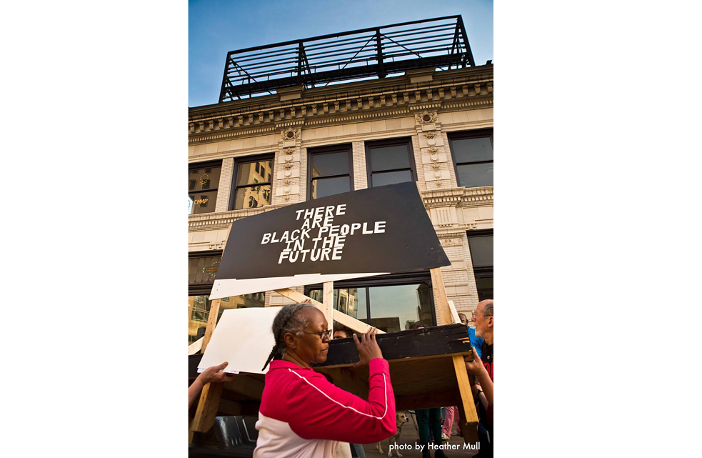 <b>„There Are Black People in the Future“ ist ein Zeichen des Protests!<b><br>Als man den Text abmontierte, veröffentlichte ich einen Kommentar dazu: Er begann als Science-Fiction-Witz eines Schwarzen Nerds. Eine Reaktion auf die Abwesenheit nicht weißer Gesichter in Science-Fiction-Filmen und Fernsehsendungen. Eine deutliche Bezugnahme auf zahlreiche Texte über den Afrofuturismus, wie beispielsweise von Florence Oyeke: „Schließlich, um den Musiker Gabriel Teodros zu zitieren: ‚Wenn wir uns nicht in die Zukunft einschreiben, werden wir auch aus dem Morgen herausgeschrieben.‘ – Der Afrofuturismus wagt es, zu behaupten, dass es nicht nur Schwarze Menschen in der Zukunft geben wird, sondern dass wir diese auch erschaffen und formen werden.“ Diese Formulierung wurde zu meinem Mantra. Später entwickelte ich ein Kunstwerk, indem ich Objekte aus dem Pittsburgher Viertel Homewood von dessen Bewohner*innen sammelte (meinen Schüler*innen, Senior*innen, Leuten auf der Straße, in der Bibliothek usw.). Ich bedruckte diese Objekte mit den Worten „There Are Black People in the Future“, tauchte sie in Harz und schuf so Artefakte dieser wunderbaren Zivilisation. Das Werk ist zu einem Archiv der Fakten, Geschichten und Mythen geworden, die das apokalyptische Narrativ dieser Diaspora fortsetzen. Ich verwende den Begriff „apokalyptisch“ bewusst, denn er speist sich aus dem langsamen Verfall der Viertel Schwarzer Amerikaner. (Und dennoch gedeihen wir). Das Gesamtkunstwerk hat bereits viele Formen angenommen: Video, Installation, Street Art, Performance und nun die Anzeigetafel. In dem Moment, als Jon mich zur Mitarbeit einlud, wusste ich, was dieser Satz in East Liberty auslösen könnte. Was der Satz in dieser Stadt, diesem Land und der Welt bedeuten könnte. Welche Gespräche daraus hervorgehen könnten, welche posttraumatischen Belastungsstörungen sich damit adressieren ließen, und einfach zu sehen, wie in diesem sozialen Klima etwas so Offensichtliches postuliert wird, hat schon eine beruhigende Wirkung auf einige – auf mich. Es wird magisch, so fantastisch wie eine Prophezeiung. Dass der Satz abmontiert wurde, macht mich tieftraurig. Und dennoch tröstet mich, wie mein Pittsburgh sich erhoben hat! Ich glaube, wir alle wissen, wie sich Unbehagen anfühlt. Lasst uns Methoden erarbeiten, um diesem Unbehagen konstruktiv auf den Grund zu gehen, ohne Druck auf andere oder anderes auszuüben. Ich fühle mich nicht dazu berufen, Menschen in eine bestimmte Richtung zu stoßen. Ein Künstler, der mich inspiriert, sagte mir: „Deine Aufgabe ist es, das Denken zu fördern, nicht den Leuten zu sagen, was sie denken sollen. Gefühle hervorzurufen, nicht den Leuten zu sagen, was sie fühlen sollen.“ Wie ihr euch auch fühlen mögt, was ihr auch denken mögt, ES WIRD SCHWARZE MENSCHEN IN DER ZUKUNFT GEBEN. Letztlich ist dieser Text ein Satz, der mir nicht gehört, er ist für alle, die ihn verwenden möchten. Bitte. Nehmt ihn. Das schickte den Text um die Welt.