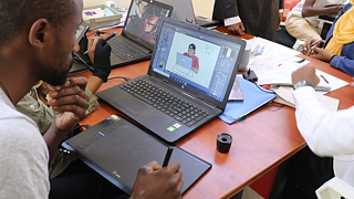 Ein Mann der über ein Tablet auf seinem Laptop eine Comicfigur zeichnet.