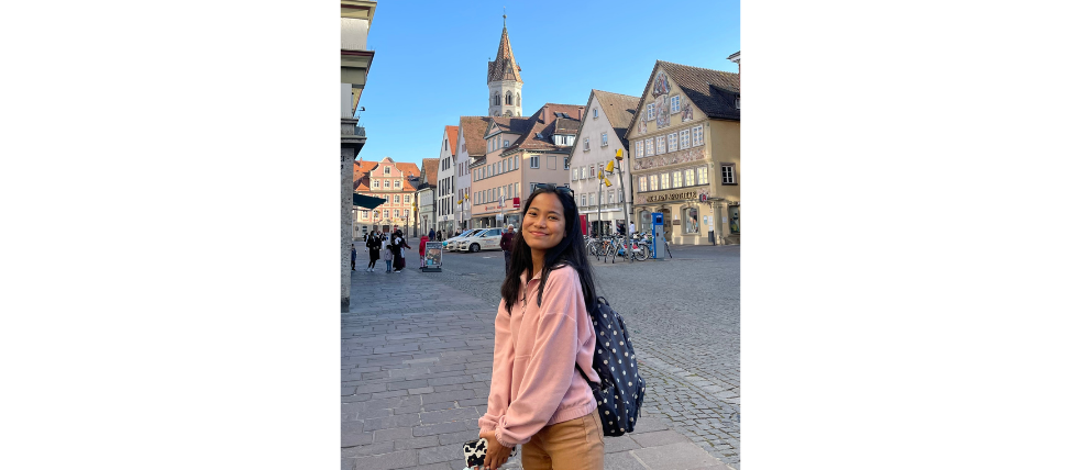 Smiling young woman with backpack on the street, behind her you can see half-timbered houses.