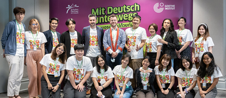 A group of people pose in front of a wall with text.