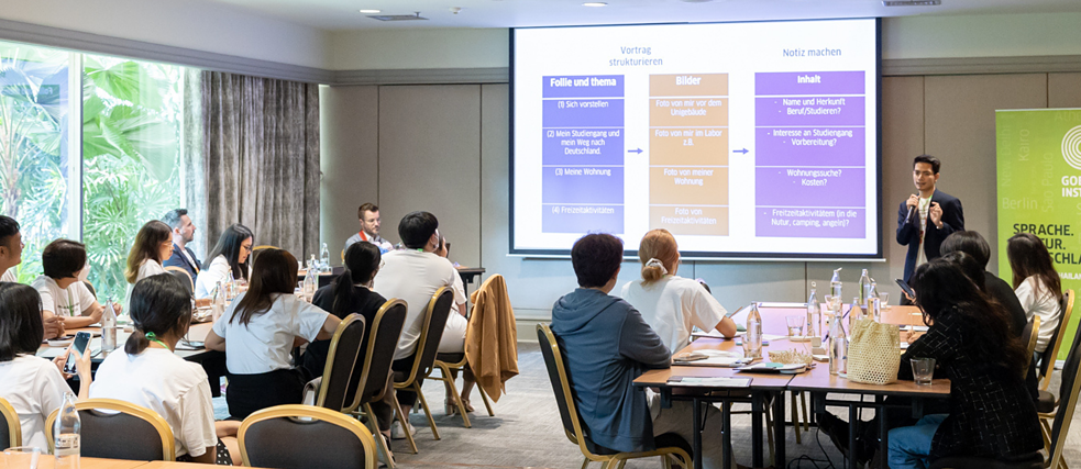 People in a hall following a lecture, screen presentation with text.
