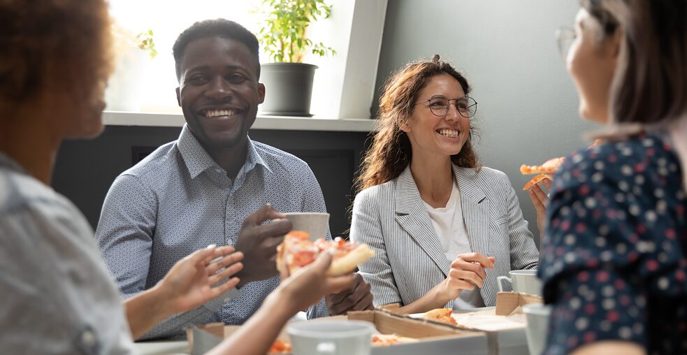 Eine Gruppe junger Menschen sitzt lachend zusammen und isst Pizza.