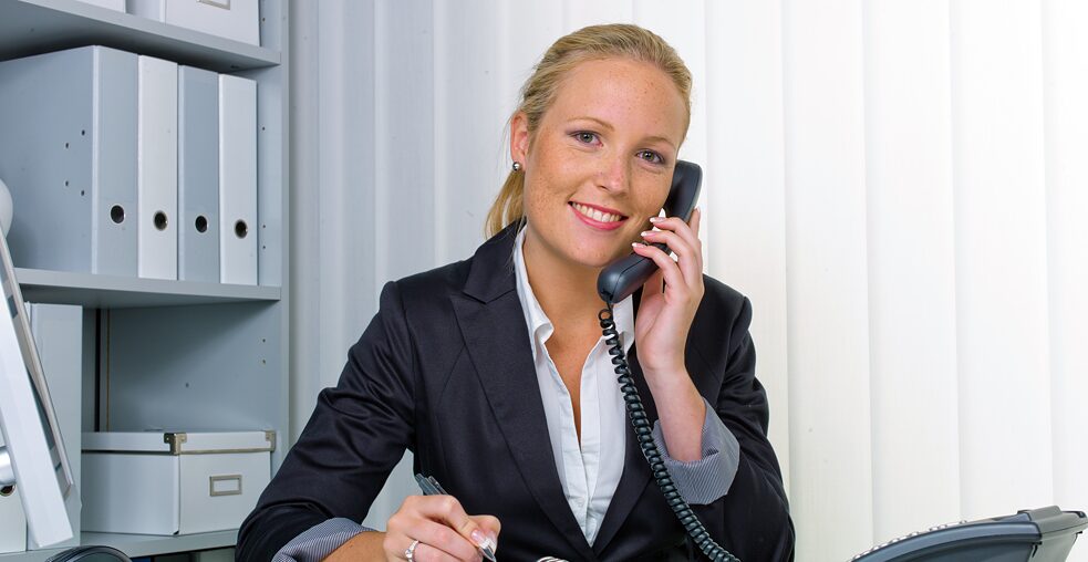 Eine junge Frau sitzt an einem Schreibtisch und telefoniert.