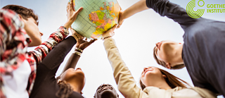 Several young people together hold a globe in the air. Shot from below against the sky.