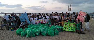 A group of people on the beach, holding up posters for environmental protection, in front of them bags filled with rubbish.