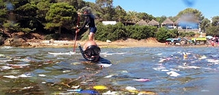 Ein Stehpaddler und ein Taucher im Wasser nahe des Ufers umgeben von Müll