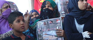 Close-up of a group of people holding a sign with images of people and arabic writing, protesting for their right to water.