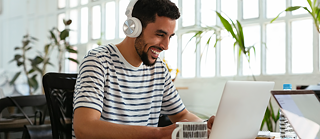 Ein fröhlicher junger Mann mit Kopfhörern lernt Deutsch am Laptop.