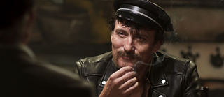 Un home amb jaqueta de cuir somriu i fuma