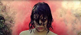 Still Frame from the Grouper Video  “I’m clean now”: Liz Harris in the rain in front of a red smoke screen