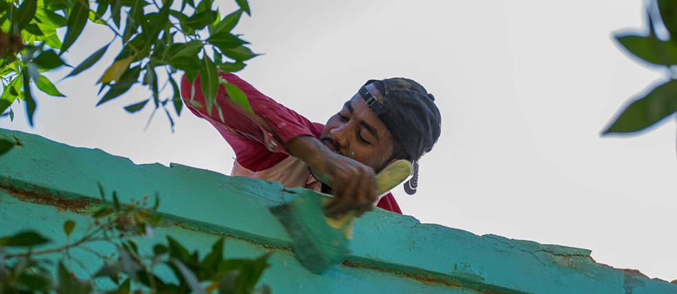 Un homme peignant un grand mur de briques vert pastel, rose et jaune.