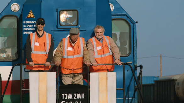 Doc Edge Festival 2022. Image from the film "The Strait Guys" showing three men in high-vis vests travelling on the front of a train.