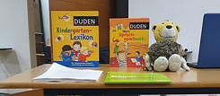 Ein Bild von zwei Duden Sprachbücher und einem Löwen Kuscheltier auf einem Tisch. Die Bücher heißen "Kindergarten-Lexikon" und "Sprachspielbuch" 